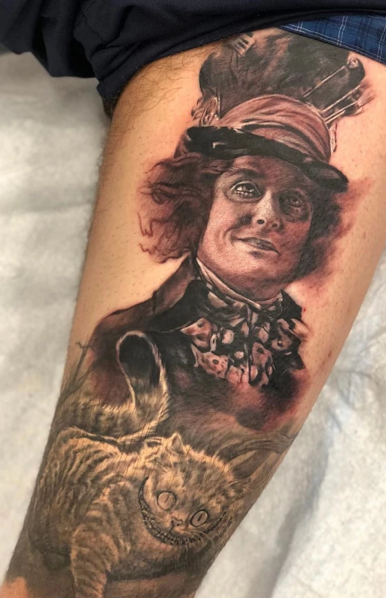 Mad hatter and cheshire cat thigh tattoo done in black and grey ink by tattoo artist Russ Howie of Sacred Mandala Studio in Durham, NC.